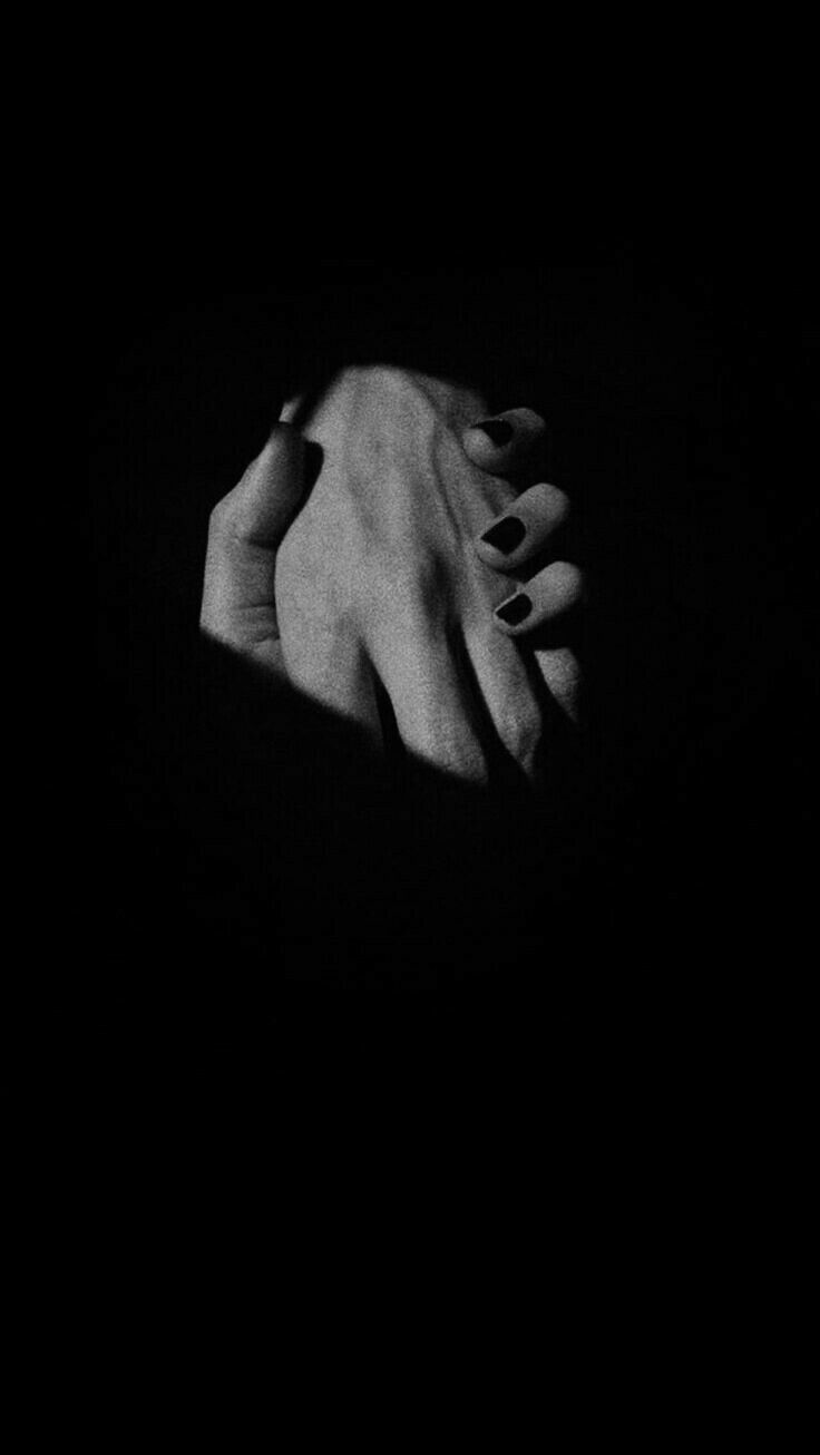 black and white photograph of two hands holding each other with their fingers in the dark