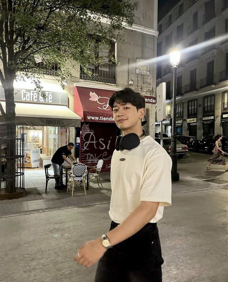 a young man standing on the sidewalk in front of a building at night, wearing headphones