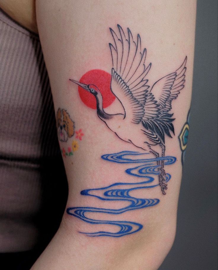 a woman's arm with a bird flying over water and the sun in the background