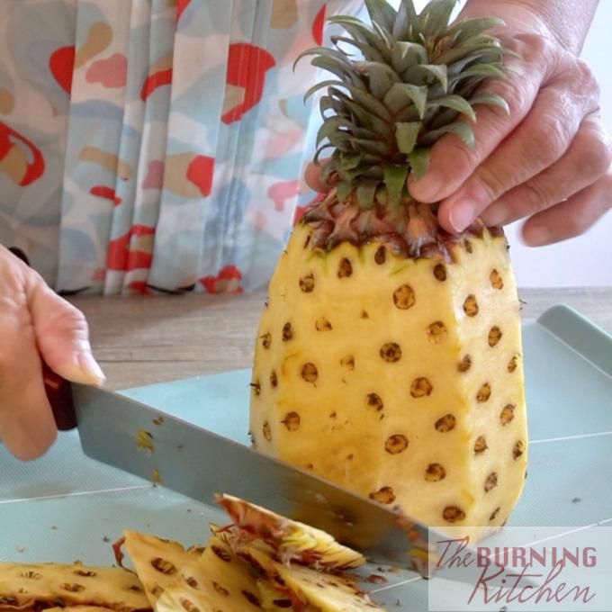 a person cutting up a pineapple on top of a blue plate with a knife