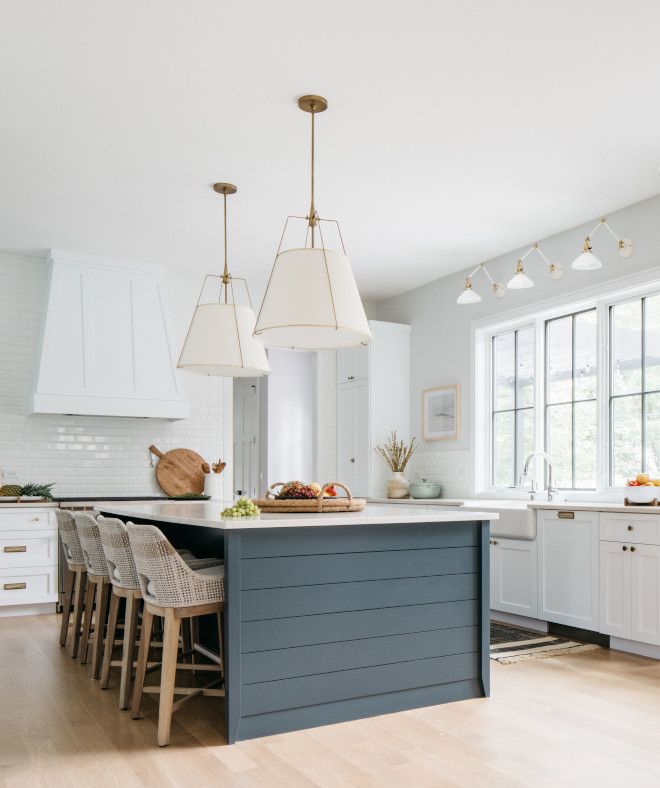 a kitchen with white cabinets and blue island in front of two windows that have hanging lights above it