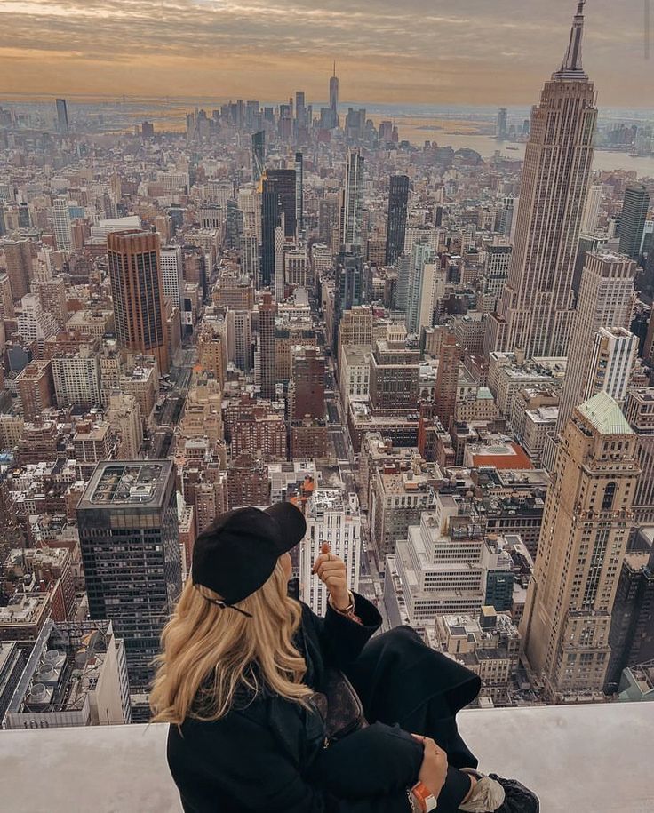 a woman sitting on top of a tall building looking down at the cityscape