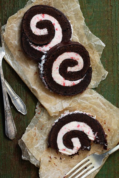 two chocolate desserts with white frosting on paper next to a fork and knife