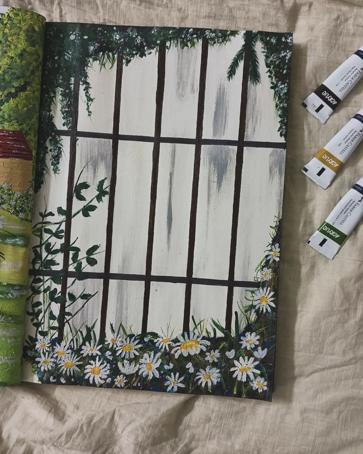 an open book with flowers on it next to some paint tubes and other art supplies