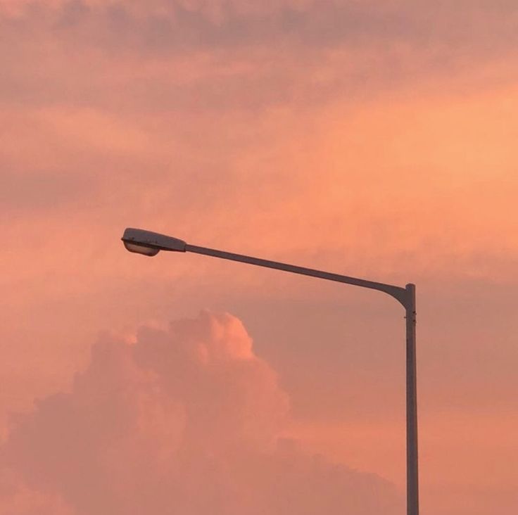 a street light on a pole in front of a pink sky with clouds at sunset