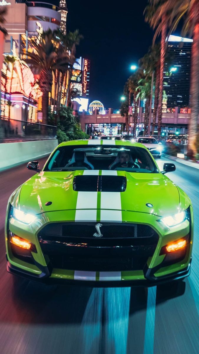 a green sports car driving down the road at night with palm trees in the background