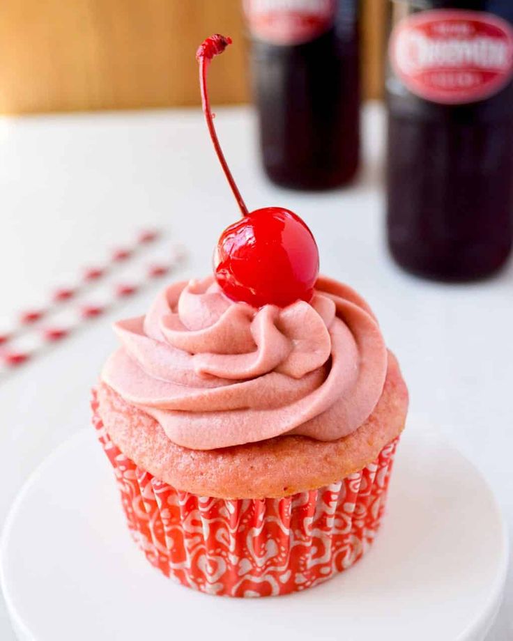 there is a cupcake with pink frosting and a cherry on top, sitting on a plate