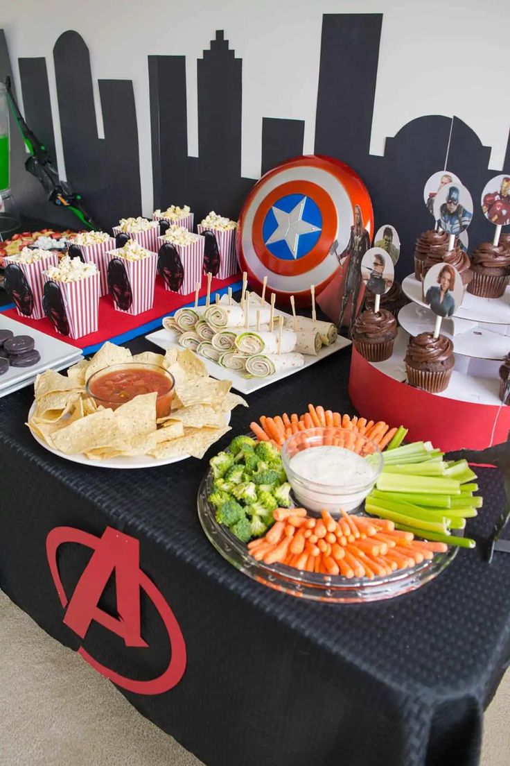 a table topped with plates of food next to cupcakes and other snacks on top of it