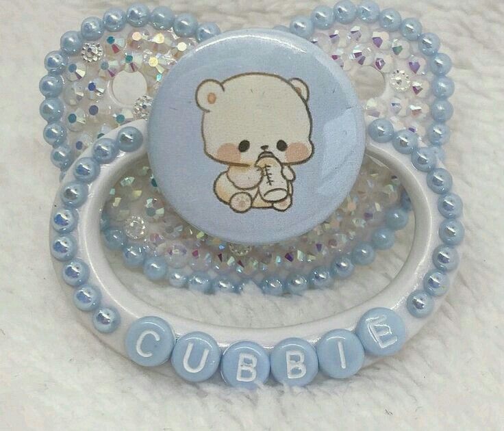 a blue and white brooch with a teddy bear on it's side, surrounded by beads