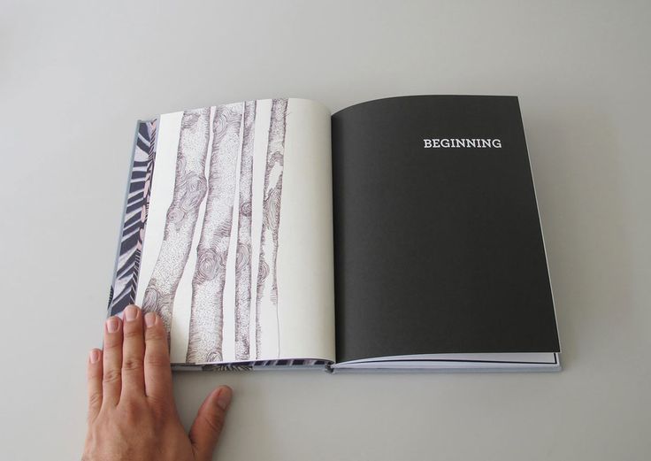 a person holding an open book on top of a white table next to a hand