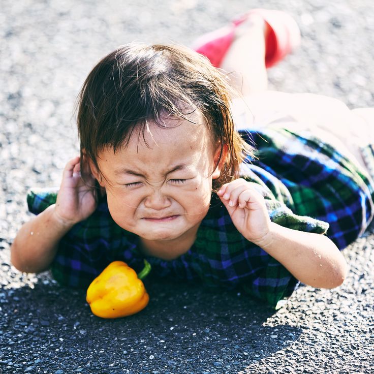 a young child laying on the ground holding a yellow pepper