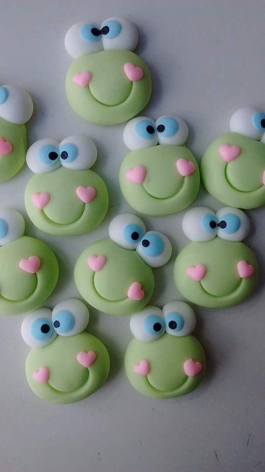 there are many green cookies with blue eyes and pink hearts on them that look like frog faces