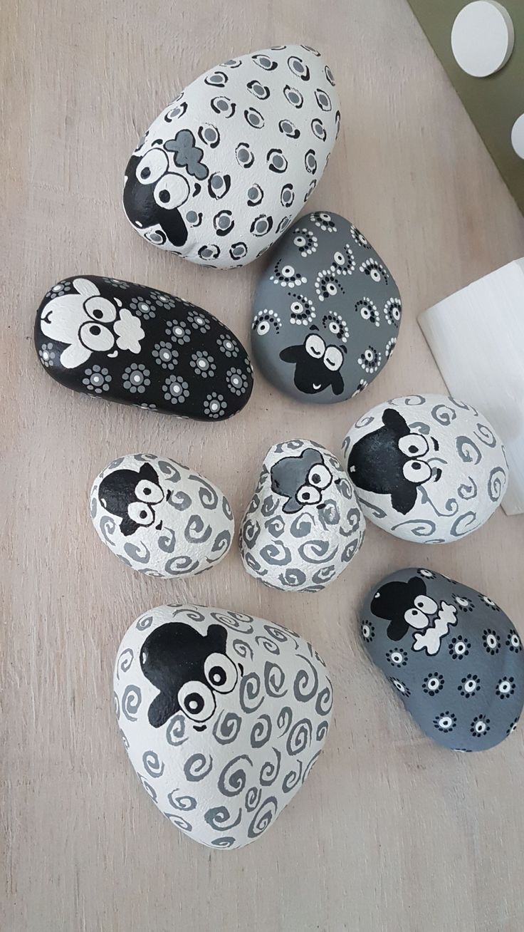 several black and white painted rocks sitting on top of a wooden table next to candles