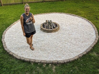 a woman standing in front of a fire pit with gravel and rocks on the ground