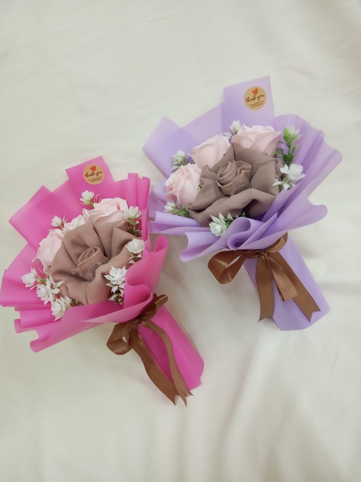 two bouquets of flowers on a bed with white sheets and pink ribbons tied around them