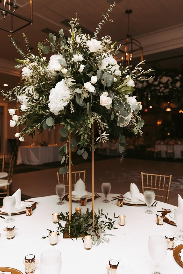 a tall centerpiece with white flowers and greenery sits on a round dining table