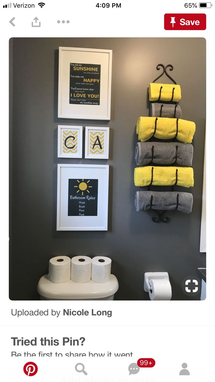 a bathroom with yellow towels hanging on the wall next to toilet paper and framed pictures