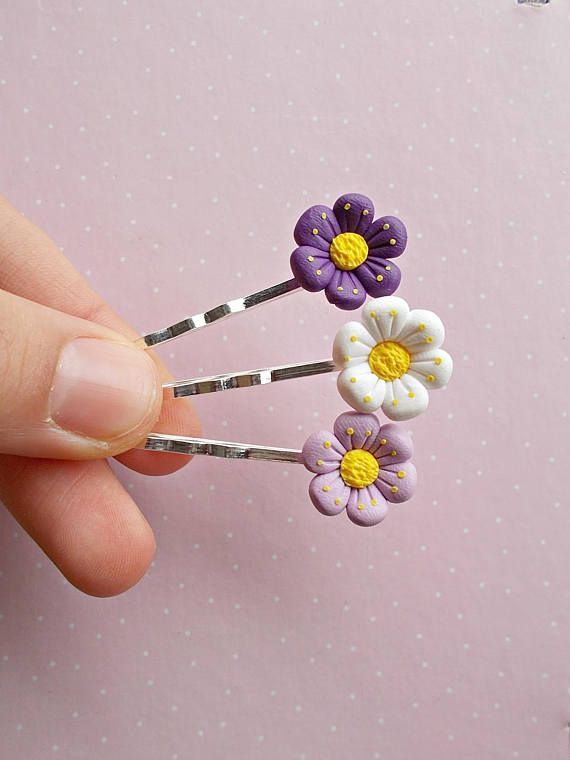 a hand holding three pins with purple and yellow flowers on them, in front of a pink background