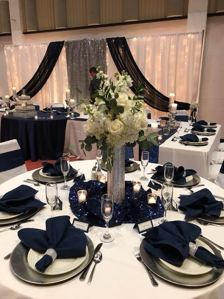 a table set up with blue and white linens, silverware, and flowers