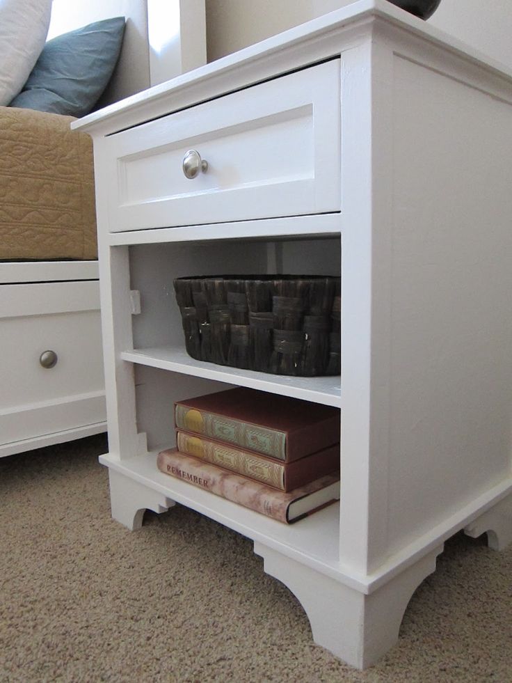 a white nightstand with books and baskets on it