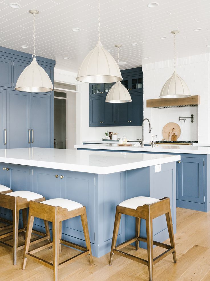 a large kitchen with blue cabinets and white counter tops, along with two stools