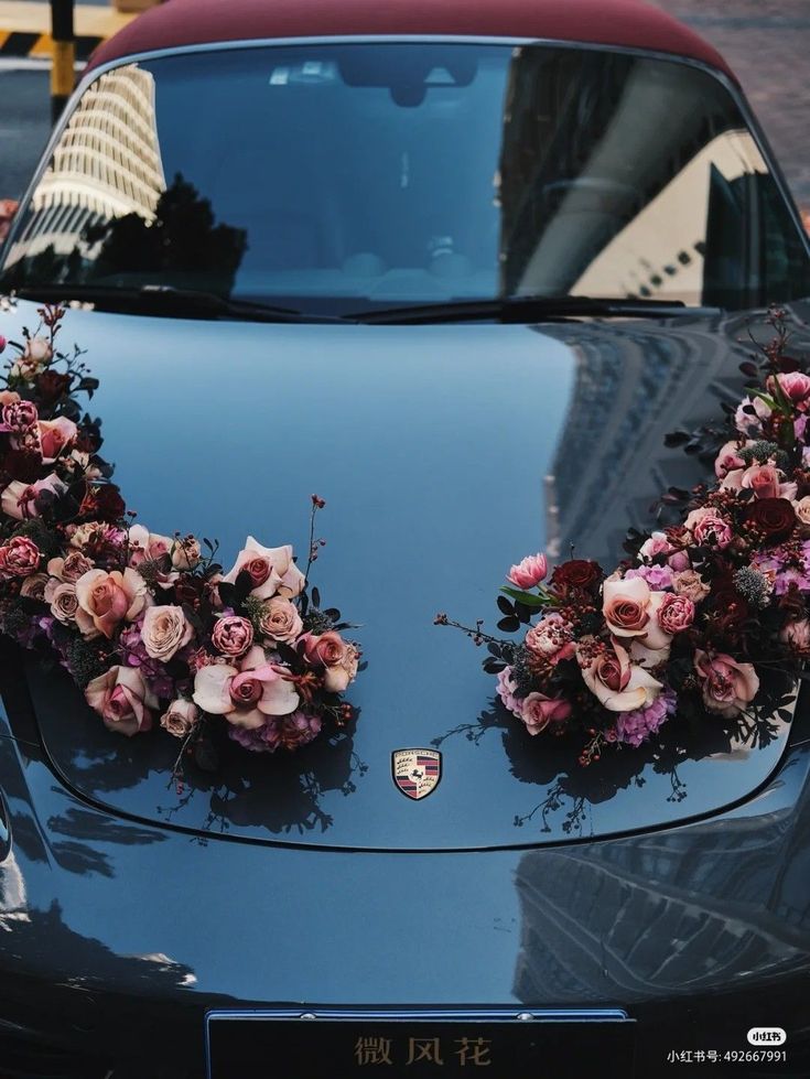 flowers are arranged on the hood of a black sports car in front of a building