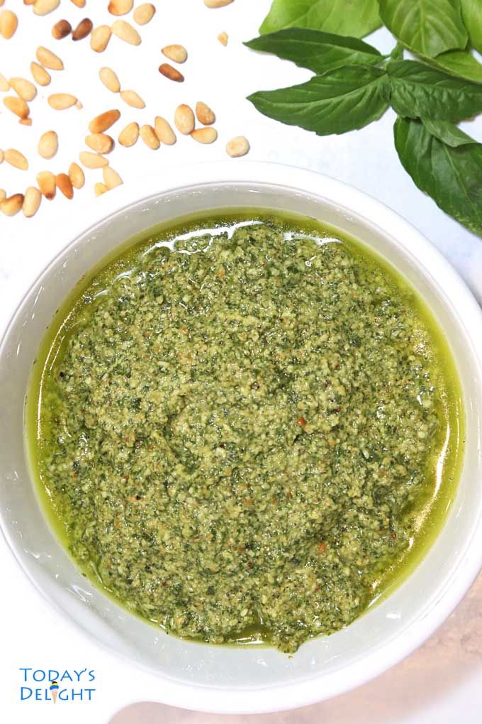 a white bowl filled with pesto next to green leaves and nuts on a table