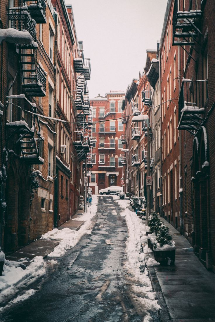 an alley way with snow on the ground and buildings in the background, during winter