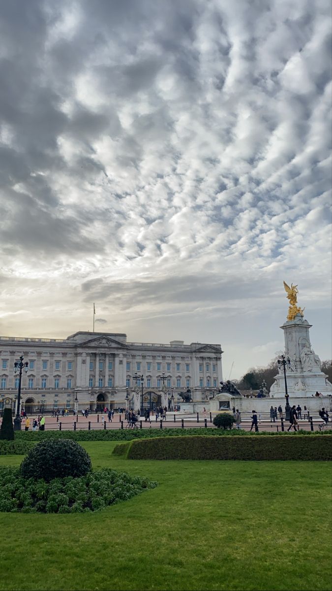 people are walking around in front of a large building with a golden statue on it