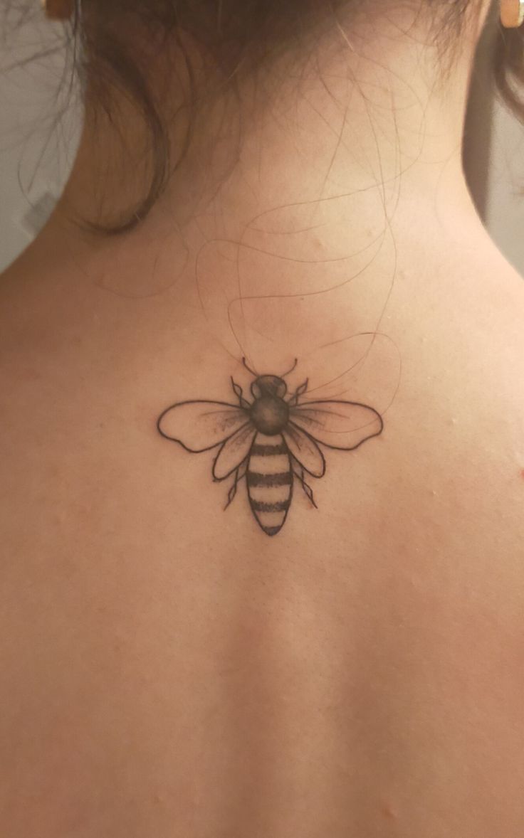 the back of a woman's neck with a bee tattoo on it