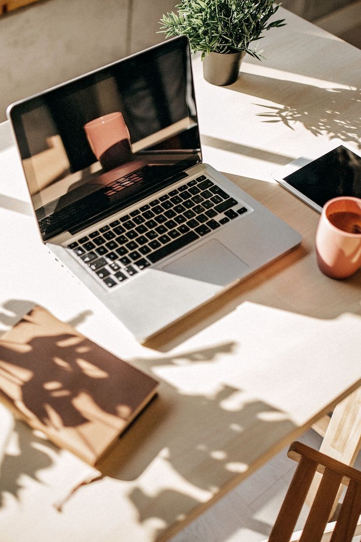 an open laptop computer sitting on top of a white table next to a cup and plant