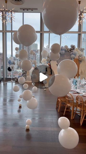 white balloons are floating in the air near tables and chairs at a party with large windows