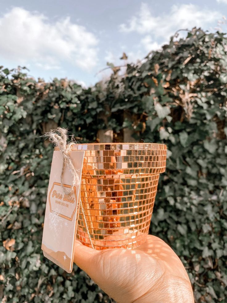 a person holding up a small cup with a tag on it in front of some bushes