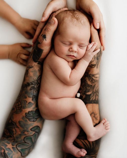 a tattooed man holding a baby in his arms