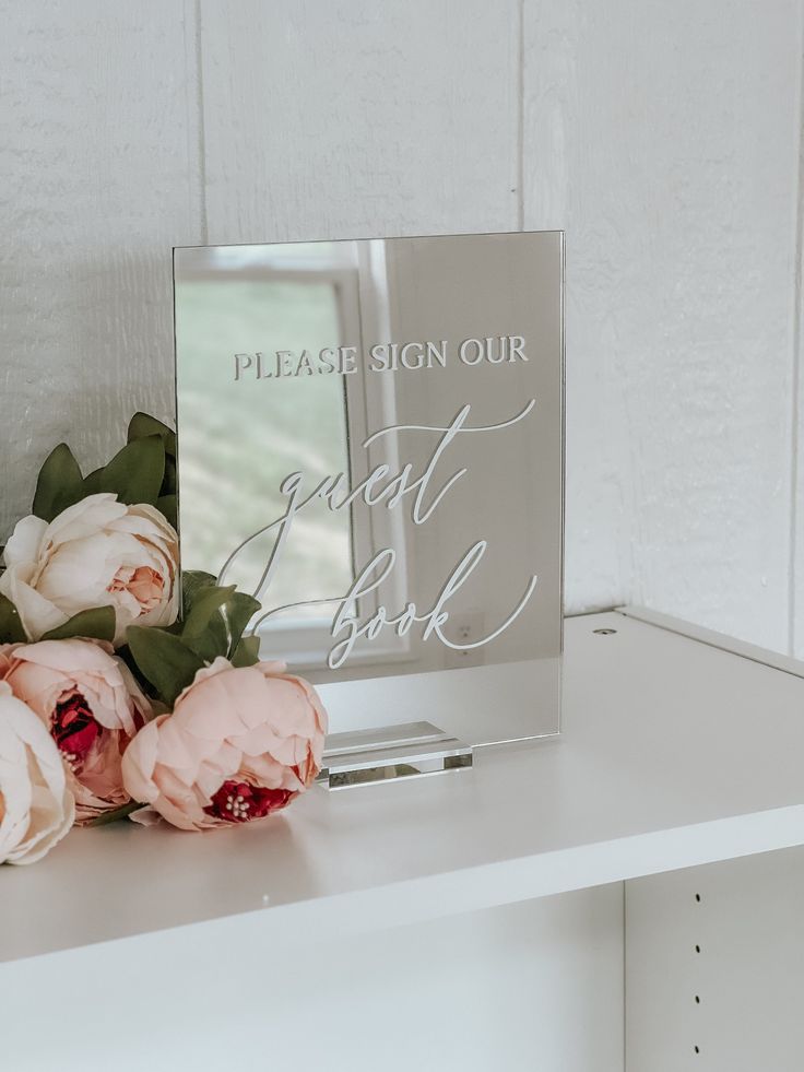 some flowers are sitting on a white shelf next to a sign that says please sign our first date