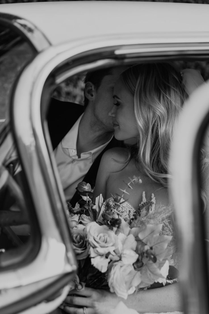 a bride and groom kissing in the back seat of a car with flowers on it