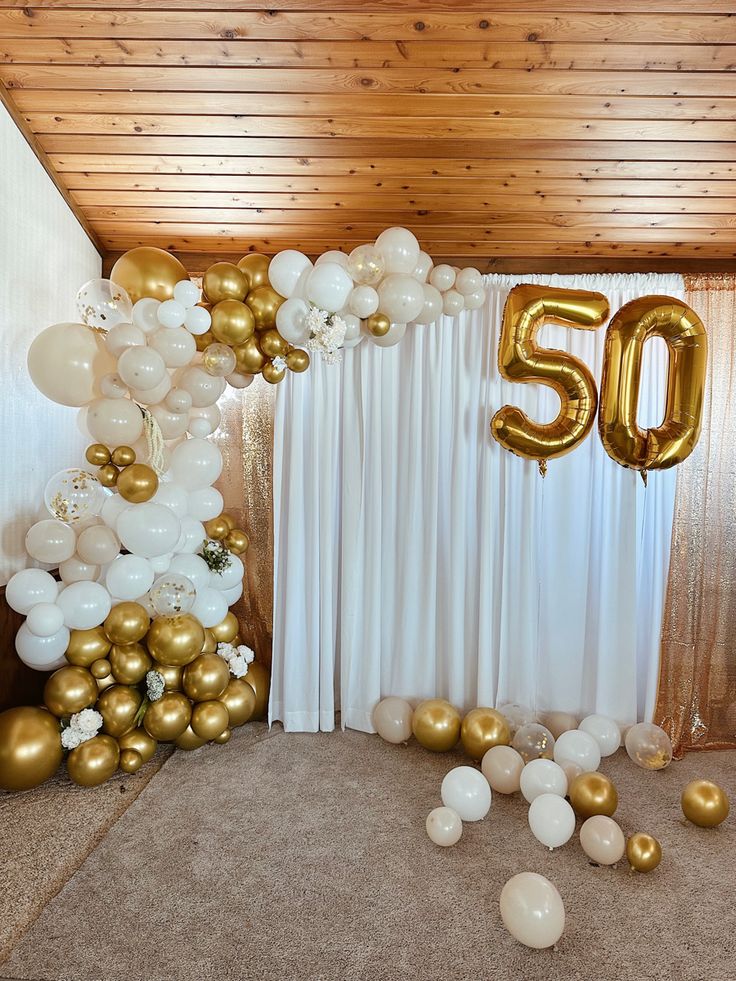 balloons and streamers are scattered around the 50th birthday balloon arch on the floor in front of white drapes