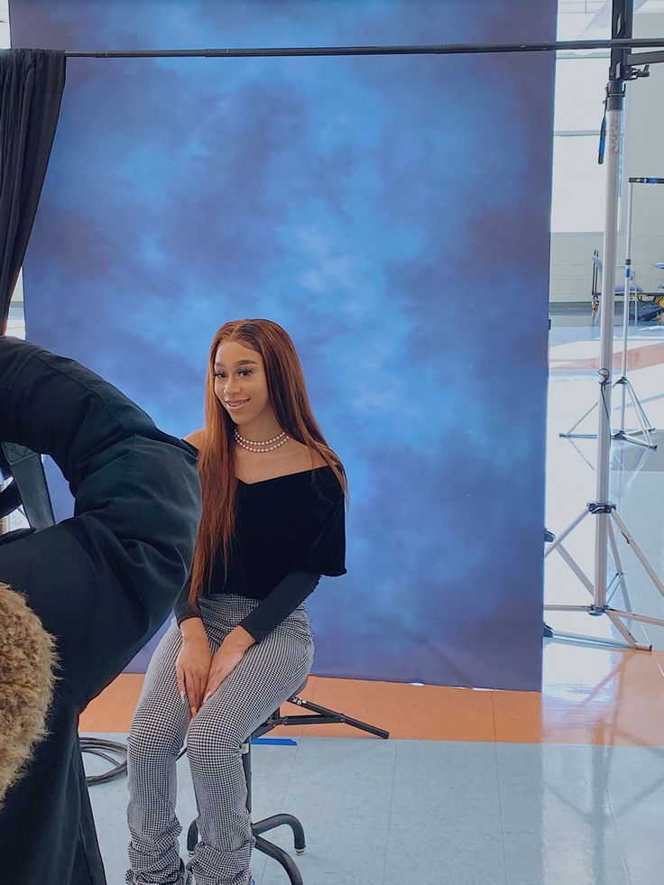 a woman sitting on top of a chair in front of a blue backdrop with lights