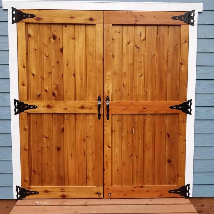 a wooden garage door with black hardware on the top and bottom panel, in front of a blue house