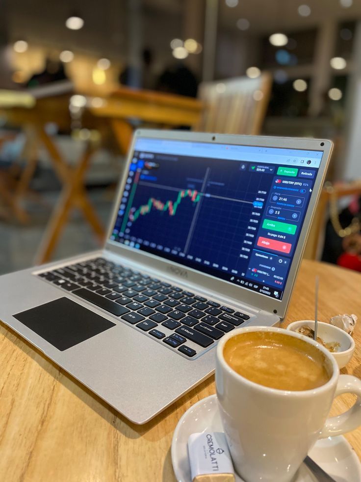 a laptop computer sitting on top of a wooden table next to a cup of coffee