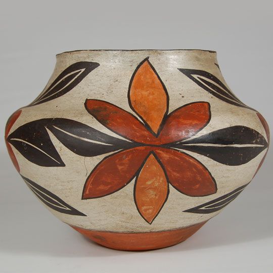 an orange and black vase with leaves painted on the side, sitting on a white surface