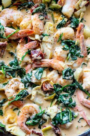 a skillet filled with shrimp, artichokes and spinach in cream sauce