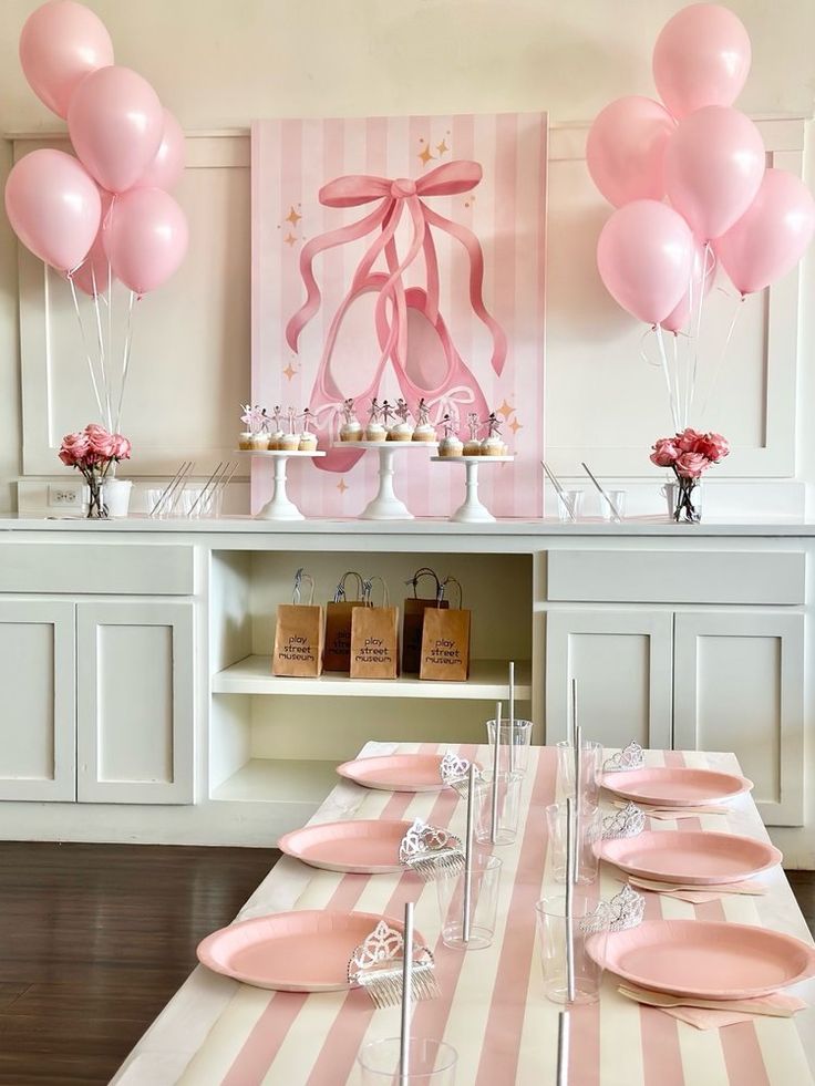 a table with pink plates and balloons on it