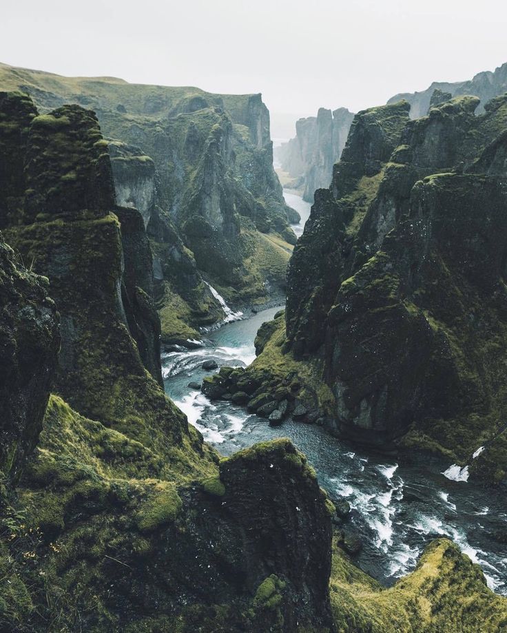 a river flowing through a lush green mountain valley next to tall rocky cliffs with moss growing on the sides