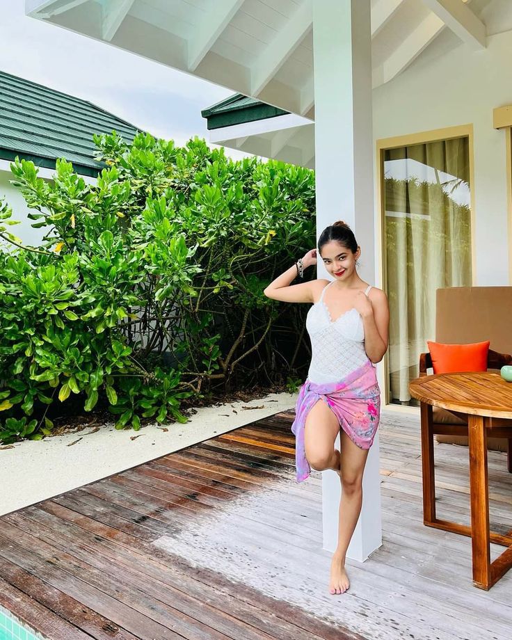 a woman standing on the edge of a wooden deck next to a swimming pool and green bushes