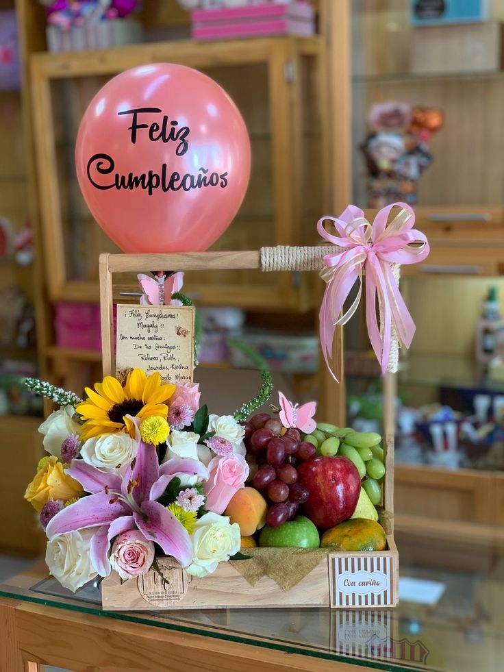 a table topped with a basket filled with fruit and flowers next to a balloon that says felig cumpleauxs