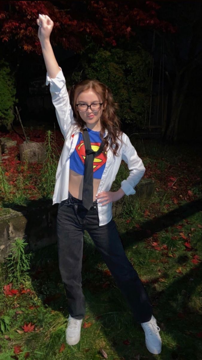 a young woman wearing a superman shirt and tie poses for the camera with her hands in the air