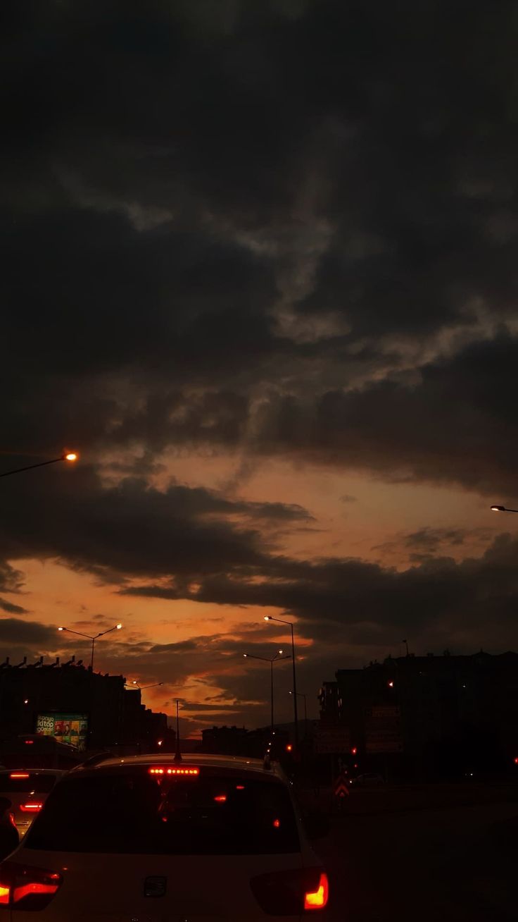 some cars are driving down the road at night with clouds in the sky behind them