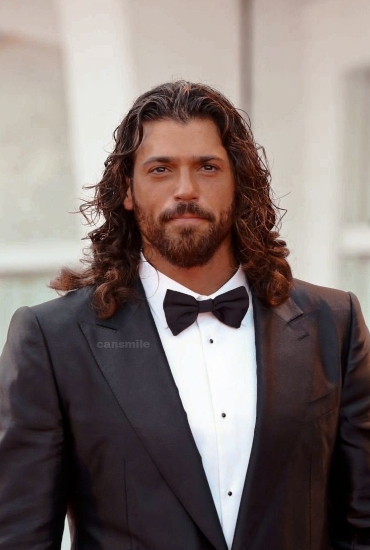 a man with long hair wearing a tuxedo and standing in front of a building