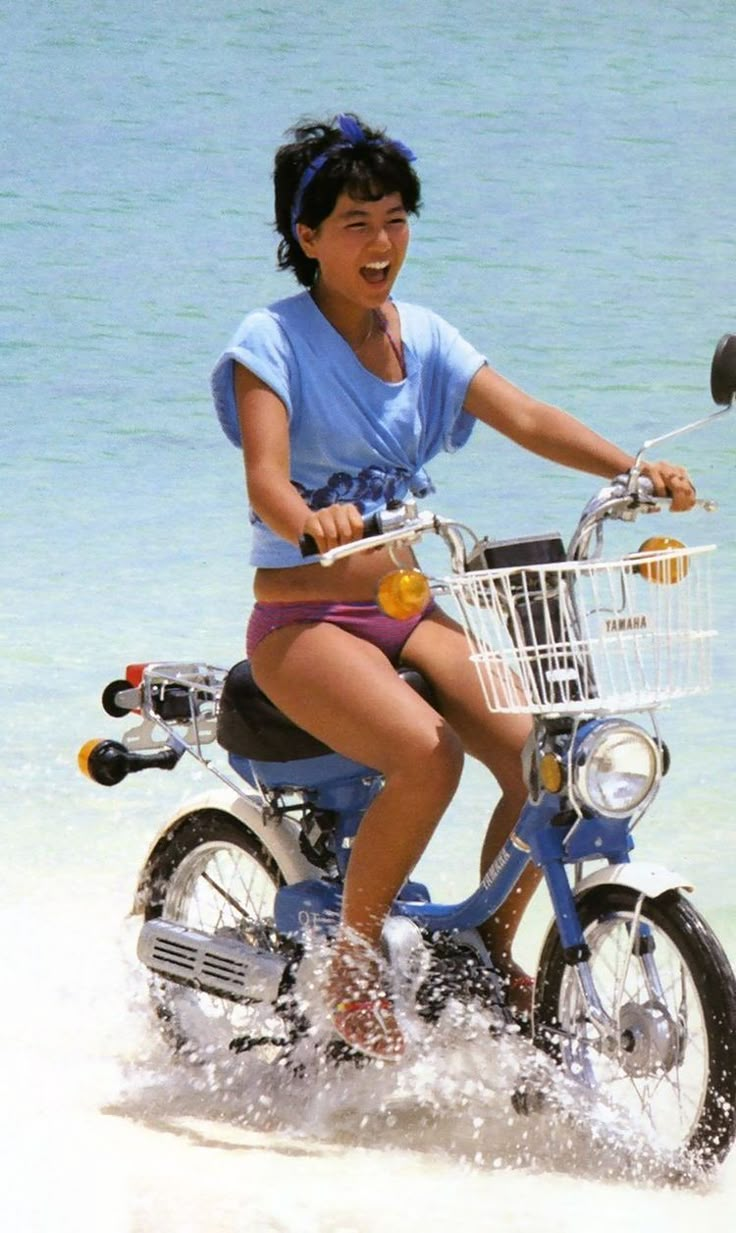 a woman riding on the back of a blue bike through the ocean water and sand